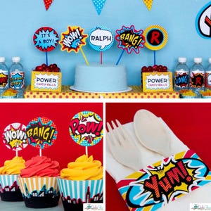 May include: A collection of comic book themed party supplies including circular cake toppers with text like IT'S A BOY, WOW, RALPH, BANG, and R, candy labels reading POWER CANDY BALLS, cupcake wrappers with city skylines, and a napkin band labeled YUM.