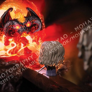 May include: A fantasy-themed image featuring a figurine facing a fiery demon. The demon is red and black with glowing eyes, wings, and a tail, set against a backdrop of flames. The figurine has light hair and is holding a sword.