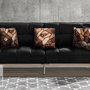 Three handmade square pillows on black suede couch made of minky fleece fabric featuring original patchwork print of multiple shades of human skin and body parts stitched together with haunted faces, ears, elbows, & nipples. Print placement differs.