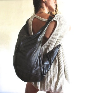 May include: A brown leather shoulder bag with a unique design. The bag is worn by a person wearing a white knitted sweater.