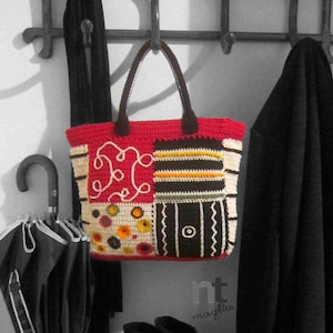 Può includere: Una borsa a mano in crochet rosso, bianco e nero con un motivo geometrico. La borsa ha un'unica tracolla ed è appesa a un gancio.
