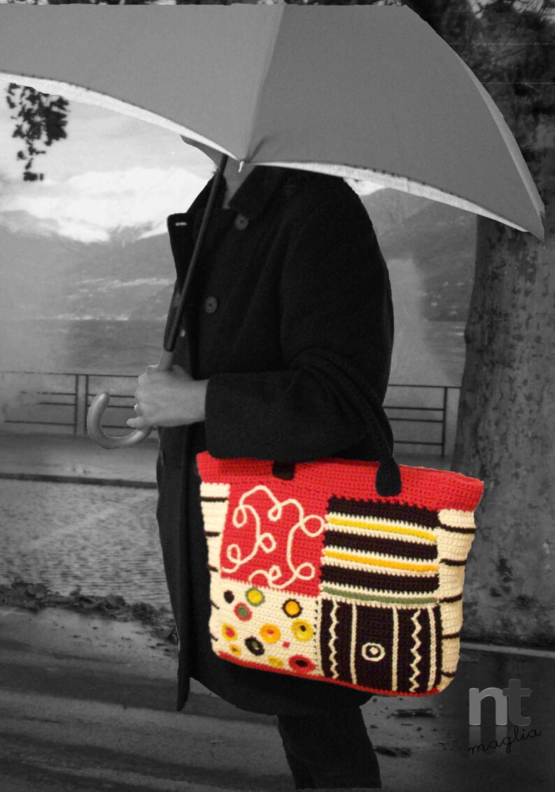 May include: A woman is walking in the rain with a black coat and a colorful crocheted tote bag. The bag has a red, white, black, and yellow patchwork design.