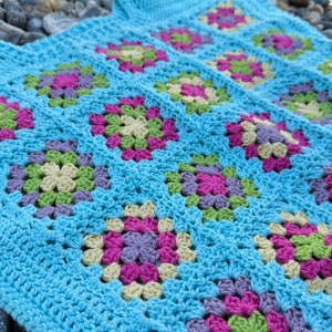 May include: A blue crochet blanket with a granny square pattern in shades of pink, green, and cream.