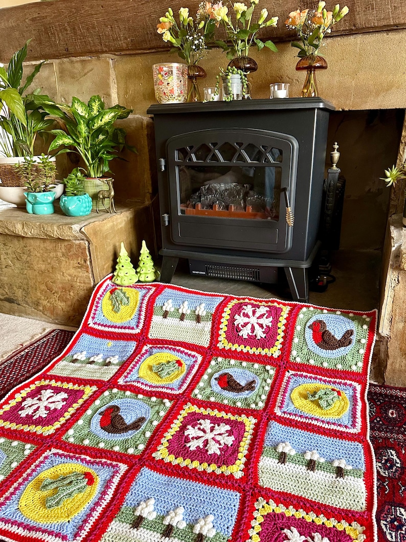 Puede incluir: Una manta de ganchillo colorida con un tema navide&ntilde;o. La manta presenta cuadrados con diferentes dise&ntilde;os, incluyendo copos de nieve, petirrojos y acebo.