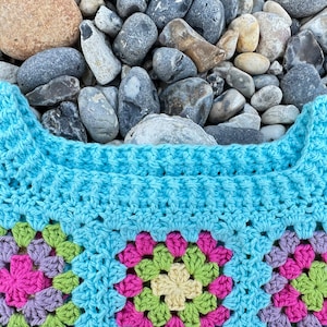 May include: A blue crocheted granny square blanket with a colourful floral pattern. The blanket is made with a variety of different coloured yarns, including pink, green, yellow, and purple.