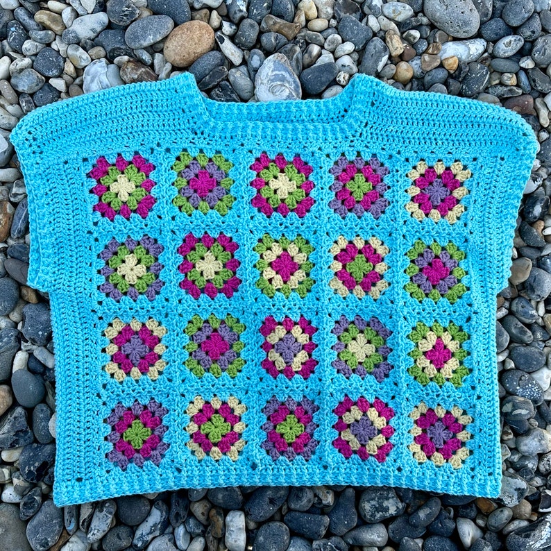 May include: A blue crochet top with a granny square pattern in shades of green, pink, and white.