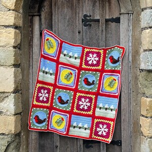 Puede incluir: Una manta de crochet roja, verde, azul y amarilla con tem&aacute;tica navide&ntilde;a. La manta est&aacute; compuesta por cuadrados con diferentes dise&ntilde;os, incluyendo copos de nieve, petirrojos, acebo y &aacute;rboles.