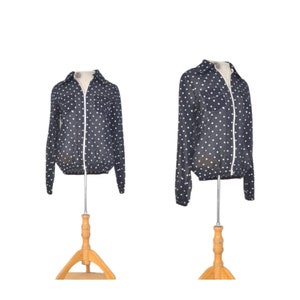 May include: A navy blue jacket with white polka dots, displayed on a wooden mannequin. The jacket has a full-length white zipper and long sleeves. The jacket is lightweight and appears to be made of a thin material.