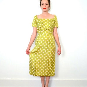 May include: A green and white polka dot dress with a scoop neck and short sleeves. The dress has a fitted bodice and a flowing skirt.