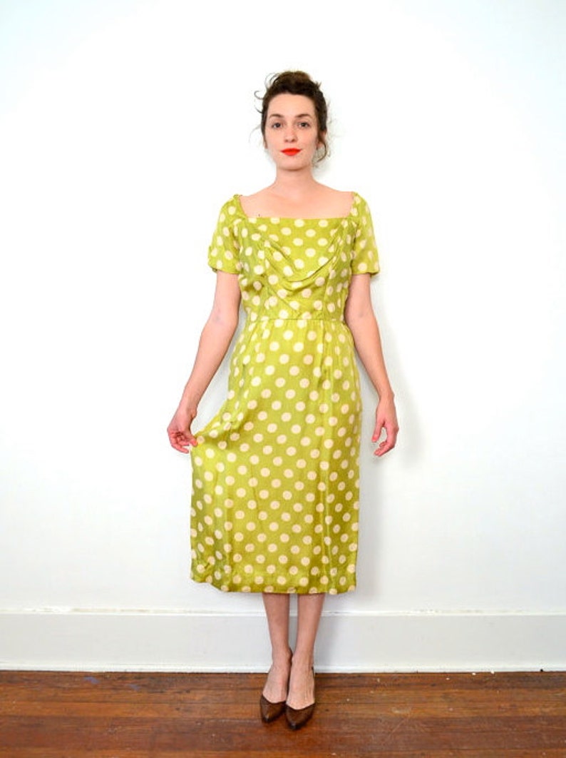 May include: A green and white polka dot dress with a scoop neck and short sleeves. The dress has a fitted bodice and a flowing skirt.