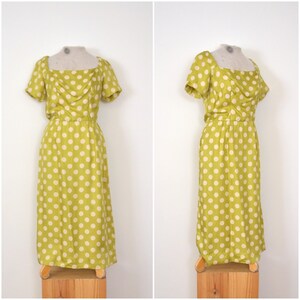 May include: A green and white polka dot dress with a square neckline and short sleeves. The dress is fitted at the waist and flows out to the hem.
