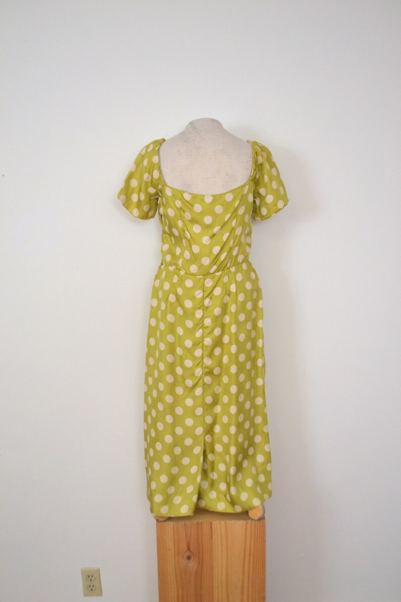 May include: A green midi dress with white polka dots. The dress has a square neckline and short puff sleeves.