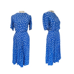 May include: A blue dress with a white floral pattern. The dress has a round neckline, short sleeves, and a fitted bodice. The skirt is full and falls to the knees.