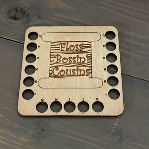 May include: Wooden floss bobbin organizer with 18 holes labeled with letters A through Q. The organizer has the text "Floss Bossin' Cousins" engraved on it.