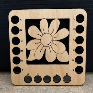 May include: Wooden yarn bowl with a flower design and 17 holes for holding yarn. The holes are labeled with letters from A to Q.