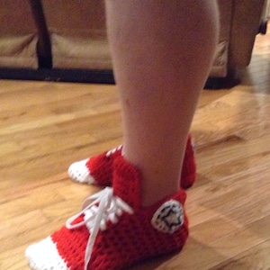 May include: Red and white crocheted slippers shaped like high-top sneakers with white laces. The slippers have a white star on the side.