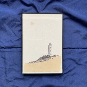 May include: Framed artwork featuring a lighthouse on a hill, rendered in black ink and watercolor. The artwork depicts a beige sand dune, a light beige sky with a yellow sun, and a black frame. The style is minimalist and evokes a coastal theme.