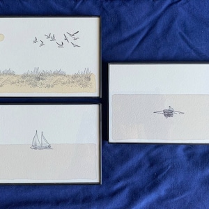 May include: Three framed black and white ink drawings of seascapes. The top drawing shows a flock of birds flying over a sandy beach with a small sun in the sky. The middle drawing shows a small boat with a person rowing in the middle of the ocean. The bottom drawing shows a sailboat on the ocean.