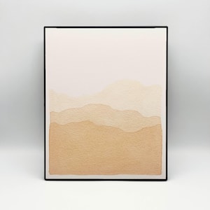 Pode incluir: Pintura em aquarela emoldurada com um design de paisagem minimalista. A obra de arte apresenta um gradiente de tons bege e castanho, representando formas onduladas em camadas que lembram colinas ou montanhas. A pintura está envolta em uma moldura preta.