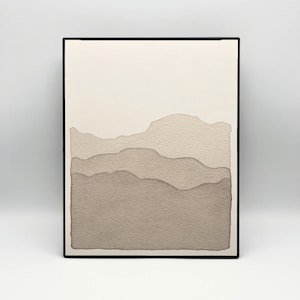 May include: A framed watercolour painting depicting a layered mountain landscape in beige and brown tones. The artwork has a minimalist style with a black frame, suitable for home decor.