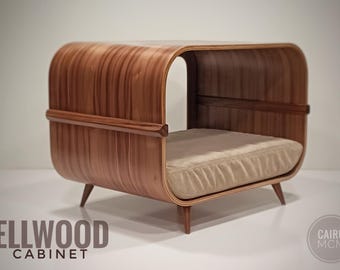 May include: A curved wooden pet bed with a smooth, polished finish and visible grain patterns. The structure features a horizontal support bar and four tapered legs, with a beige, rectangular cushion placed inside the open frame.