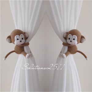 May include: Two brown crocheted monkey curtain tiebacks with white faces and white arms holding onto white curtains. The text "Solutions 25/1" is visible in the bottom center of the image.
