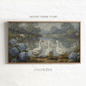 Op de afbeelding: Een ingelijst landschapsschilderij met drie witte ganzen bij een meer. Blauwe hortensia's en andere vegetatie omlijsten de scène. De tekst "INSTANT FRAME TV ART" en "COLOR ZEN" zijn zichtbaar.