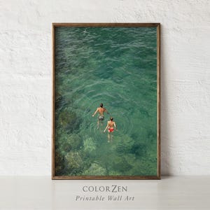 May include: Printable wall art featuring a top-down view of two people swimming in clear turquoise water. The artwork is framed in a brown wooden frame. The text "COLORZEN Printable Wall Art" is at the bottom.