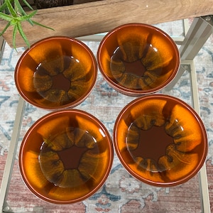 May include: Four brown ceramic bowls with a mottled glaze pattern. The bowls are arranged in a square shape on a glass surface.