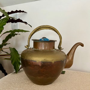 May include: A vintage copper and brass teapot with a blue and white enamel lid. The teapot has a rounded body and a curved spout.