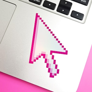 May include: A pixelated computer mouse cursor sticker featuring a white center with a vibrant hot pink outline. The sticker is applied to the silver surface of a laptop keyboard area, positioned below the command, option, and shift keys.