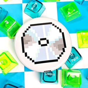 May include: A white button with a pixelated CD design, surrounded by colorful keyboard keys. The keys are transparent and in shades of green and blue, scattered on a blue and white checkered surface. The button has the text "@RIPYR".