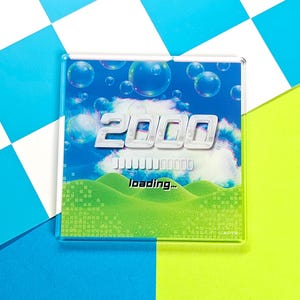 May include: A clear, square acrylic magnet with a retro design. The design features the number "2000" in white, a loading bar, and the word "loading..." against a backdrop of a blue sky with bubbles and green hills.