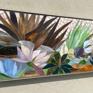 May include: A rectangular stained glass mosaic wall art featuring a variety of plants and flowers in shades of brown, green, blue, pink, and purple.