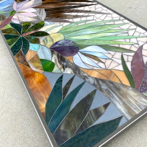 May include: A rectangular mosaic artwork featuring a variety of colors and textures, including green, brown, purple, and white. The mosaic depicts a stylized floral design with leaves and flowers.