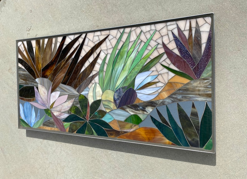May include: A colorful mosaic wall art featuring a variety of plants and flowers. The artwork is made of small pieces of glass in shades of brown, green, blue, purple, and white.