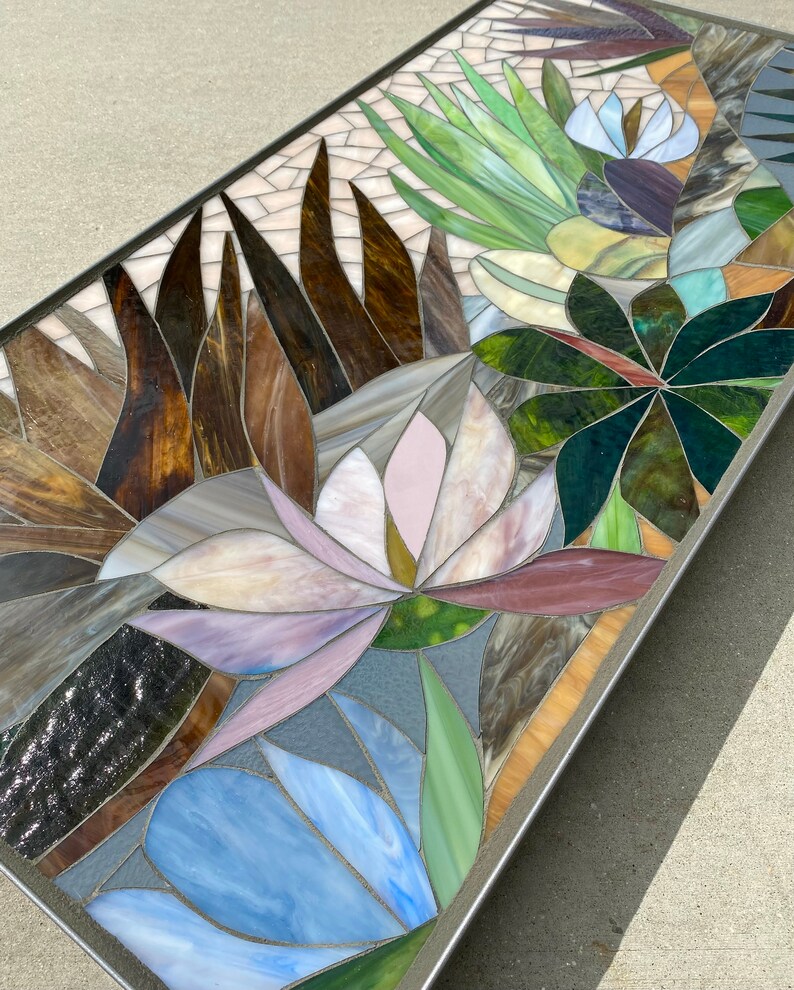 May include: A rectangular mosaic table top with a floral design. The design features pink, blue, green, and brown glass tiles arranged in a pattern of flowers and leaves.