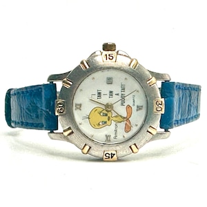 May include: A silver-toned Armitron watch with a blue leather band. The watch face features the cartoon character Tweety Bird. The watch has gold-toned accents and displays the time.