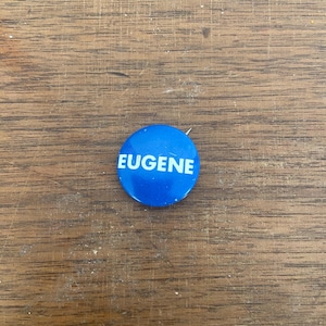 May include: A blue button with the word "Eugene" printed in white.