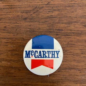 May include: A white, blue, and red political campaign button with the text "McCarthy" and a star.