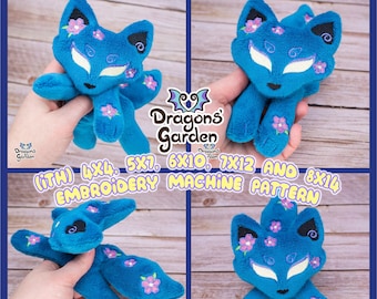 May include: A blue plush fox with pink flowers embroidered on it. The fox is sitting on a wooden surface. The text "Dragons Garden (iTH) 4x4, 5x7, 6x10, 7x12 AND 8x14 EMBROIDERY MACHINE PATTERN" is visible in the image.