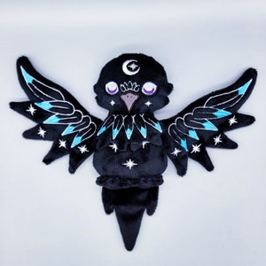 May include: Black plush toy with wings, a crescent moon on its head, and blue and white embroidery of stars and feathers.