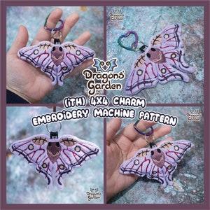 Könnte beinhalten: Gestickter Motten-Charm mit Schlüsselanhänger. Die Motte ist lavendelfarben mit dunkelvioletten und braunen Details. Der Text "Dragons Garden" und "(ITH) 4X4 CHARM EMBROIDERY MACHINE PATTERN" sind ebenfalls sichtbar.