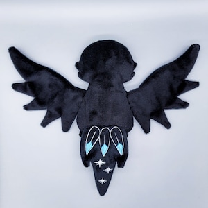 May include: Black plush dragon with blue and white embroidered details on its tail. The dragon has large wings and a small head.
