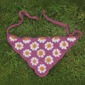 May include: A pink crocheted triangle scarf with white and yellow daisy flowers.