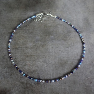 以下が含まれることがあります： シルバーの留め具が付いた、繊細なビーズチョーカーネックレス。ネックレスは、青、白、茶色の色合いの小さなカラフルなビーズが特徴です。