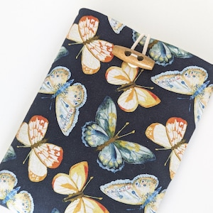 May include: A dark blue fabric book cover with a repeating pattern of colorful butterflies. The cover has a wooden button and a loop of twine.