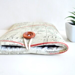 May include: A beige and brown fabric tablet case with a map print and a wooden button closure. The case is closed and the button is fastened.