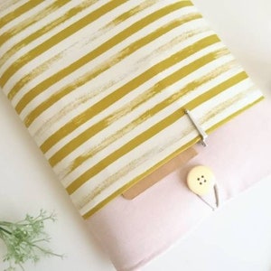 May include: A yellow and white striped fabric laptop sleeve with a pink lining and a brown cardboard insert. The sleeve has a small button and a metal clip.