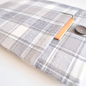 May include: A gray and white plaid laptop sleeve with a brown leather flap and a wooden button closure.